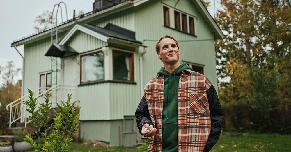 Nuori mies omakotitalon edessä avaimet kädessään 