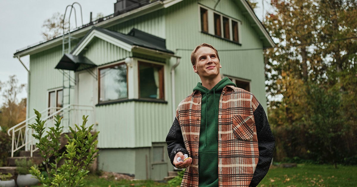 Nuori mies omakotitalon edessä avaimet kädessään